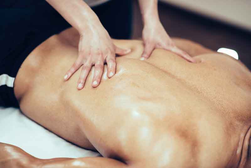 Massage therapist massaging lower back region of a male athlete