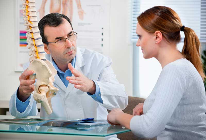 Physical Therapist shows the problem areas on the model of the spine to the patient and explains the cause of her pain